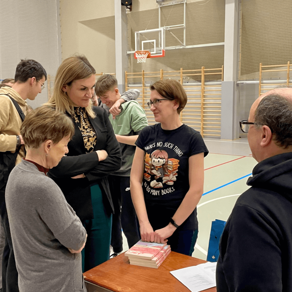 Spotkanie autorskie w Liceum na Górce, na zdjęciu Lena Klimka rozmawiająca z kilkoma nauczycielami, a w tle uczniowie liceum i technikum