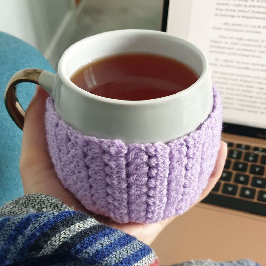 Kubek z herbatą w dłoni, w tle ekran komputera, zdjęcie ilustrujące ćwiczenia na rozruch pisarski