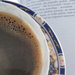 Zbliżenie na filiżankę czarnej kawy w ozdobnej, granatowo-złotej porcelanie, stojącą obok otwartej książki. Zdjęcie symbolizuje analogowy odpoczynek i antidotum na FOMO