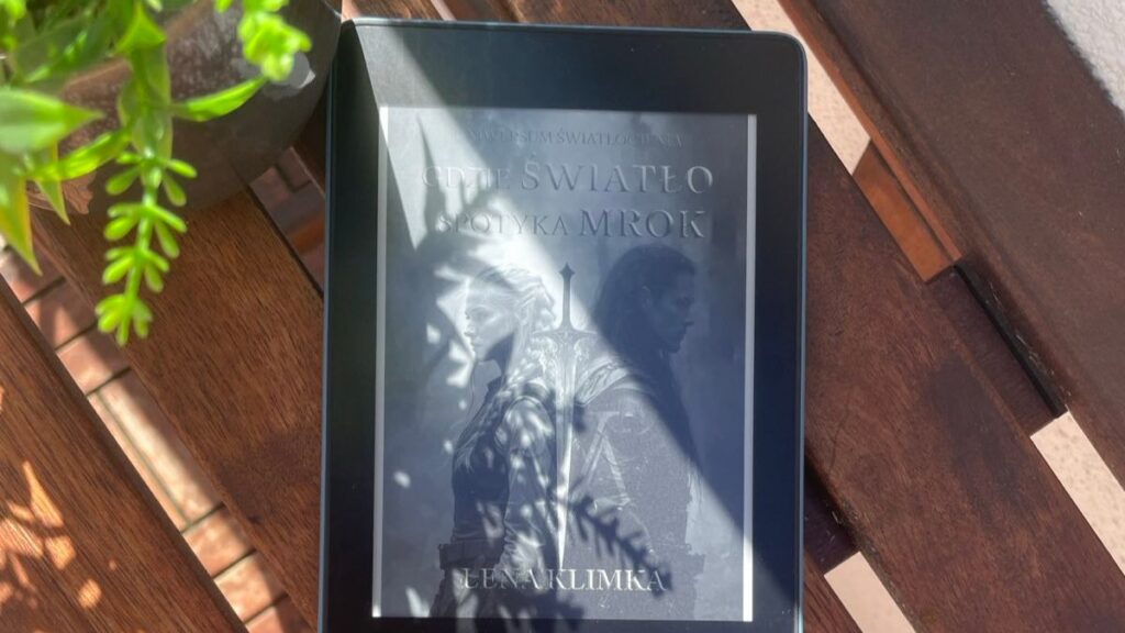Czytnik ebooków na drewnianym stole z okładką książki Leny Klimki „Gdzie Światło spotyka Mrok” – dystrybucja książki w self-publishingu.